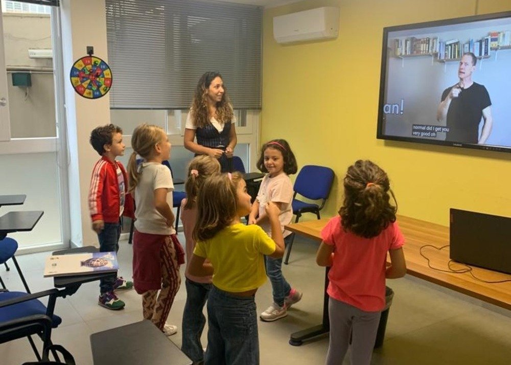 La docente Divina sta insegnando inglese ai bambini in una aula gialla.